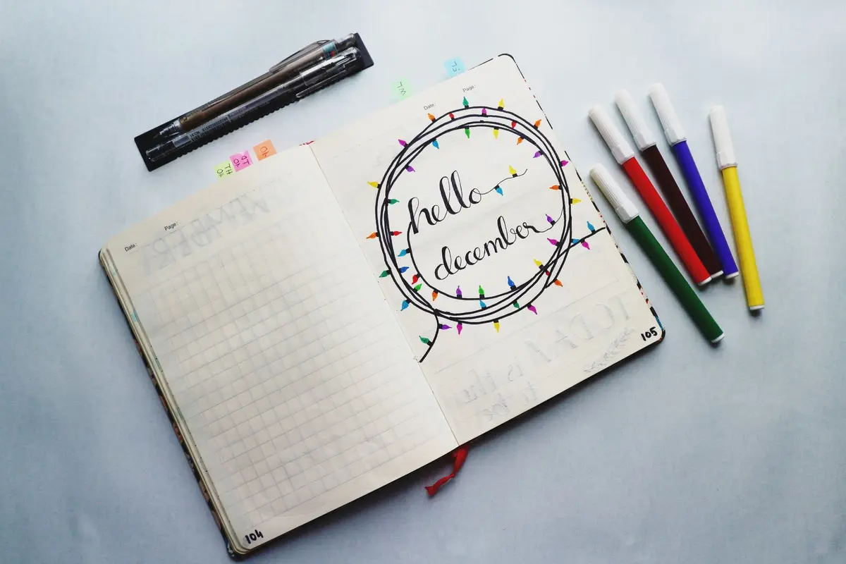 An open planner decorated with hand lettering, color coded page tabs, and a row of colorful markers beside it