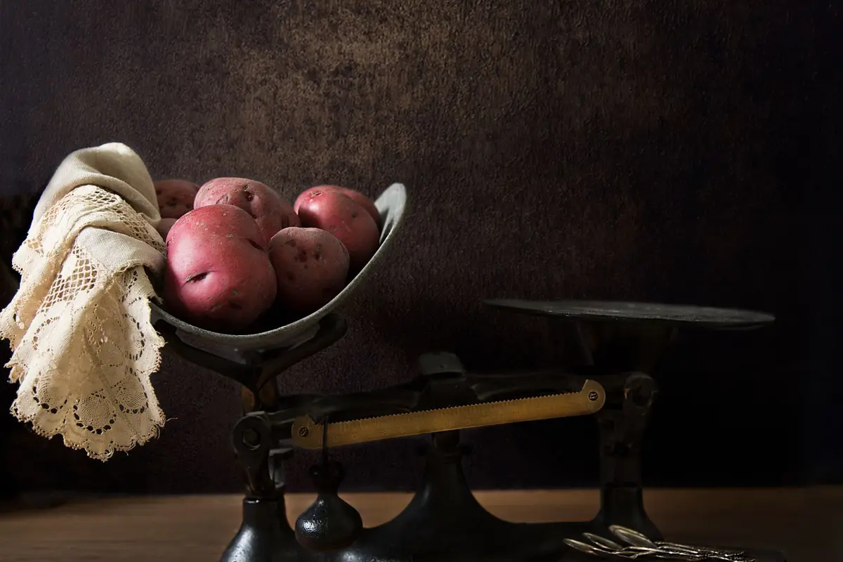 Red potatoes piled on one pan of an antique cast iron balance scale on a wooden table