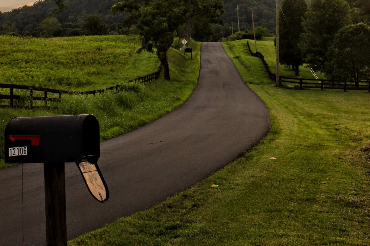 Classic rural mailbox with a red flag beside a winding country road at dusk