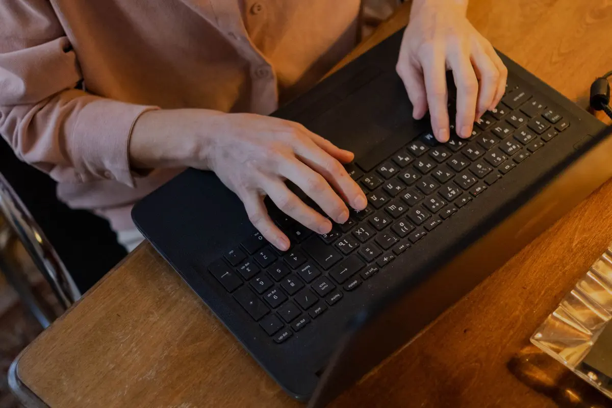 Hands typing on a laptop at a worn wooden table in warm evening light