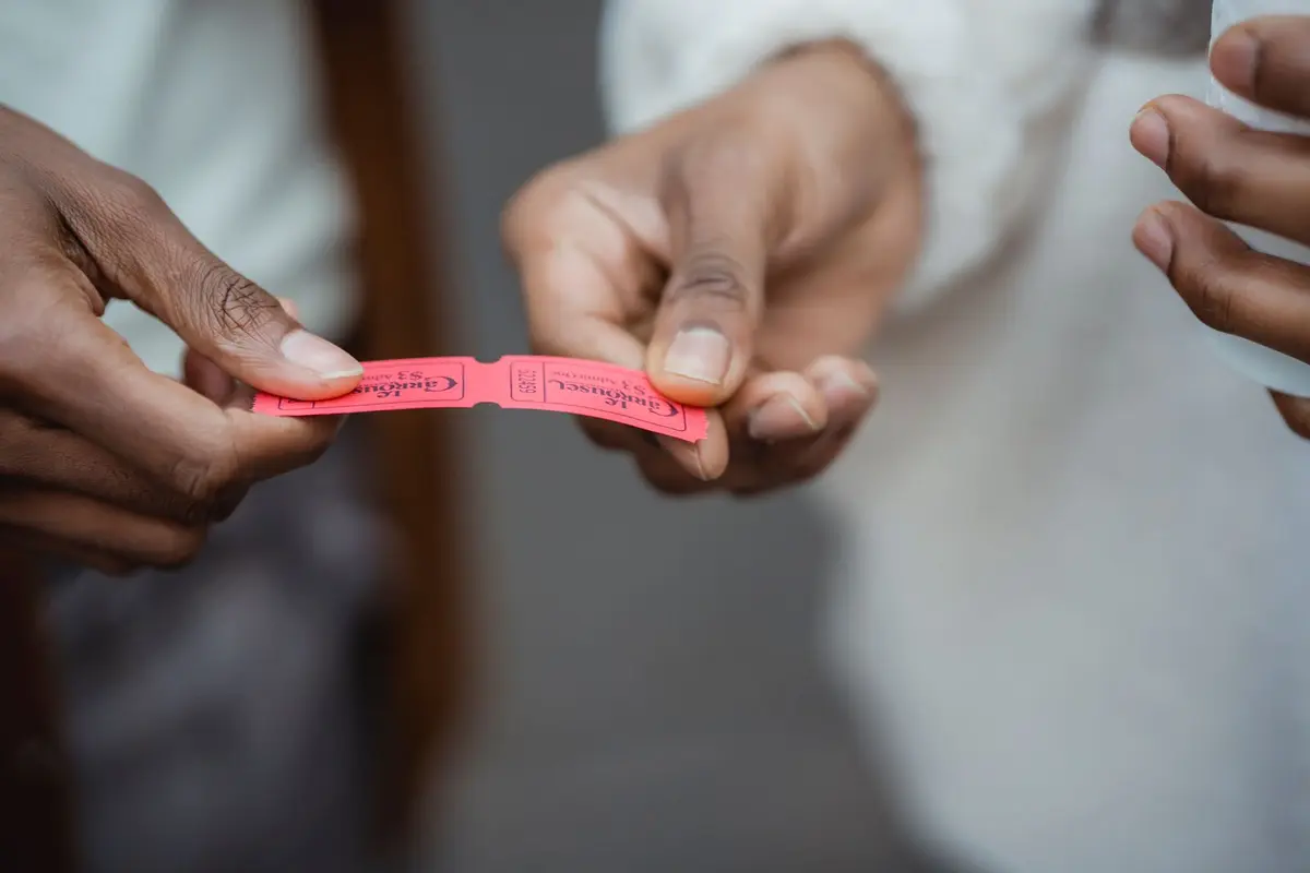 Close-up of one person handing a red paper admission ticket to another at an event