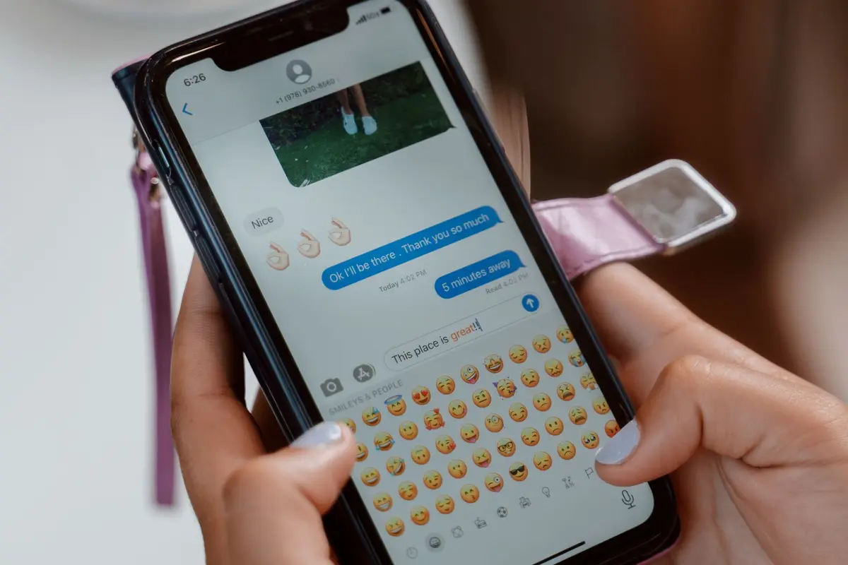 Hands holding a smartphone in soft natural light, with a friendly text conversation open on the screen