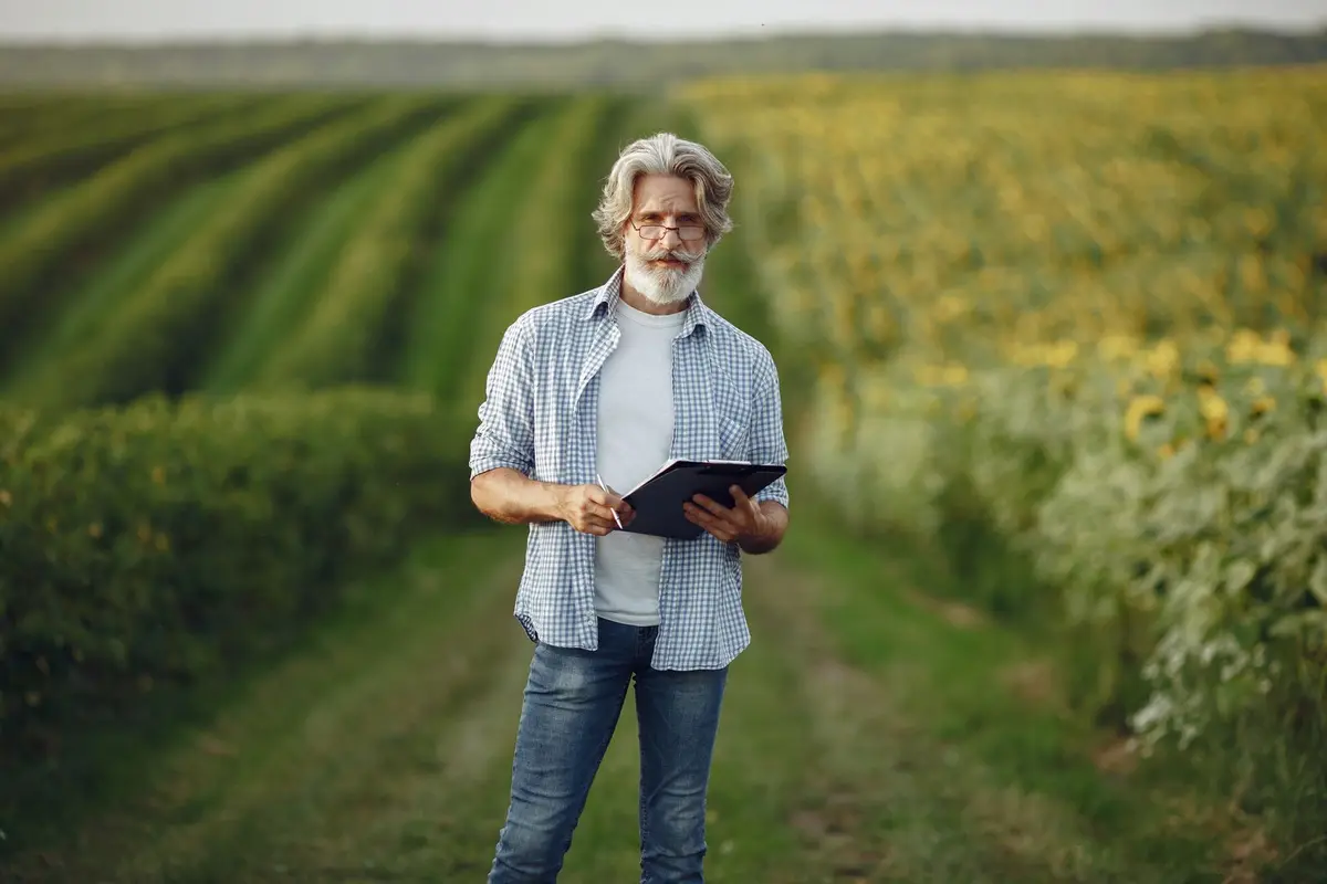 A farmer standing between green crop rows, reviewing his season setup on a tablet