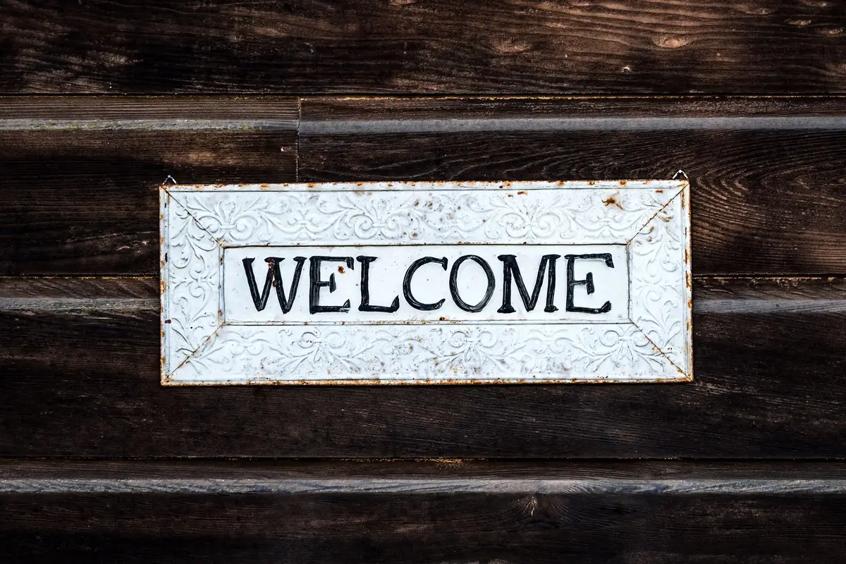 Rustic white metal welcome sign hanging on a dark wooden barn wall